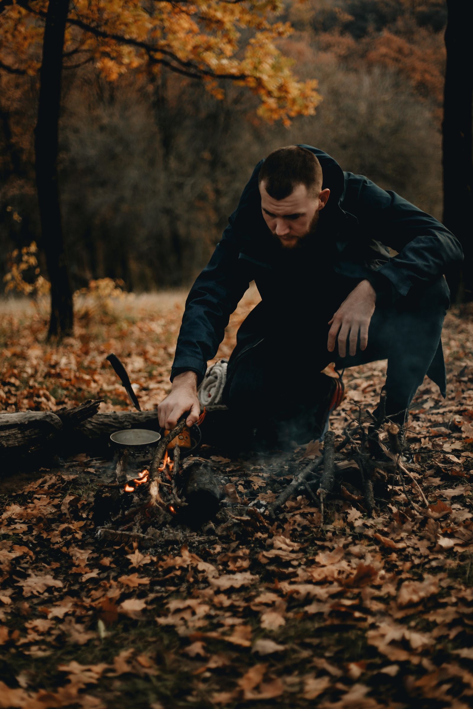 A man makes a fire in the autumn forest and warms ash over the flames