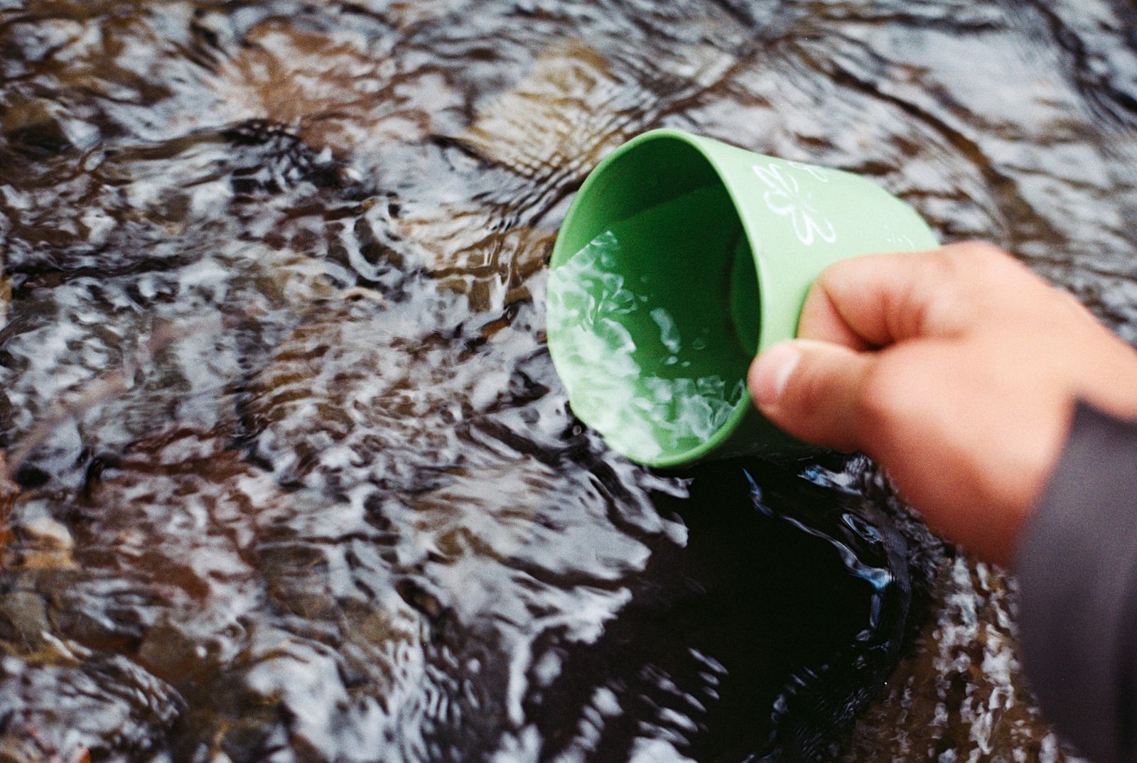 Taking water with a green mug from a flowing stream in nature