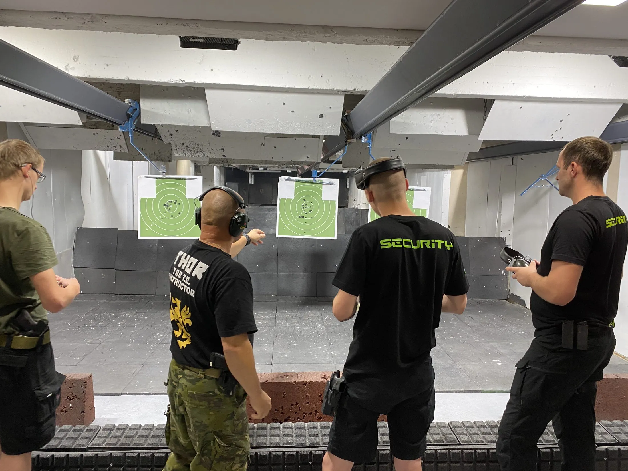 Skupina cvičenců střílí z pistolí na kryté střelnici